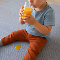 Bambino che beve un succo d'arancia sulla Passatoia Cucina Genia Beige, con una macchia di succo sul pavimento.